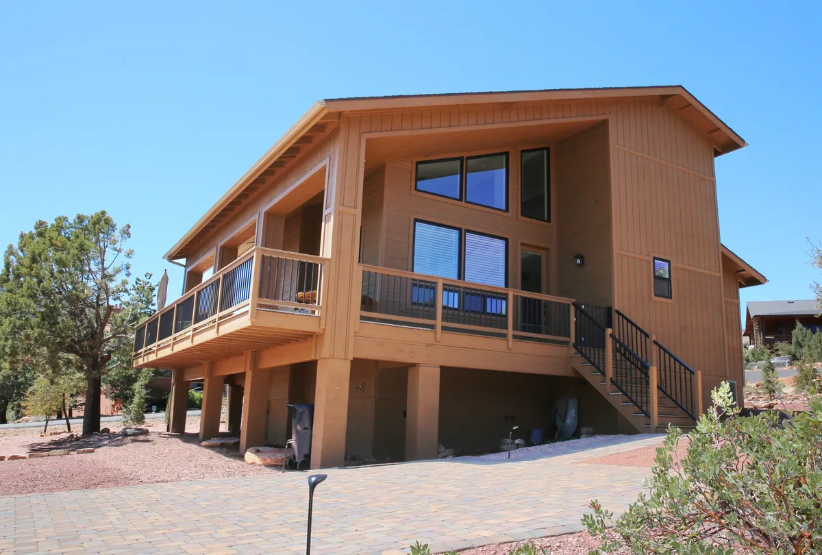 The exterior of the modern mountain home features large windows, an elevated deck, and a wooden facade surrounded by trees. The deck offers space for outdoor dining and relaxation, with a sense of privacy and immersion in nature. The mood is welcoming and serene, ideal for romantic getaways.