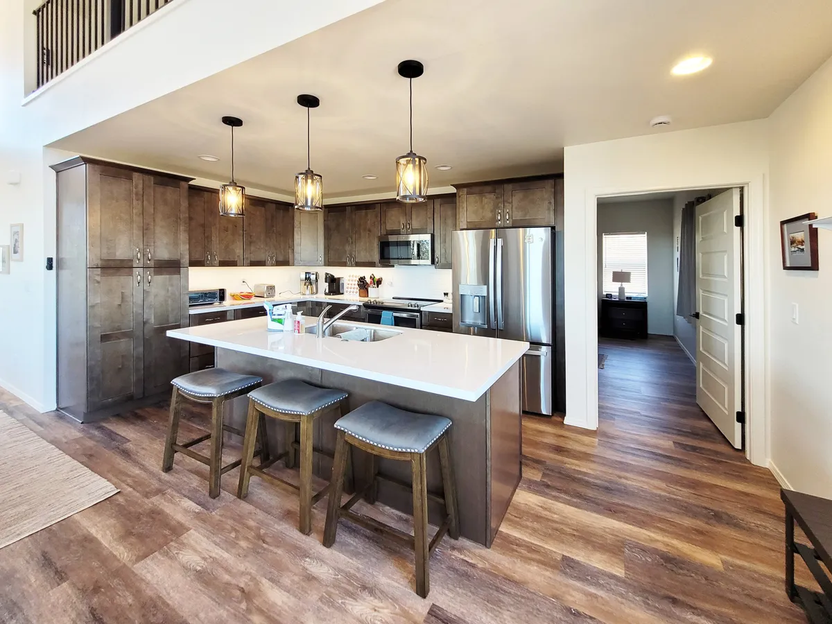 A welcoming kitchen scene featuring an island with bar stools, kitchen cabinets, and stylish pendant lights. The layout encourages both cooking and casual dining, capturing a sense of family activity and gathering.