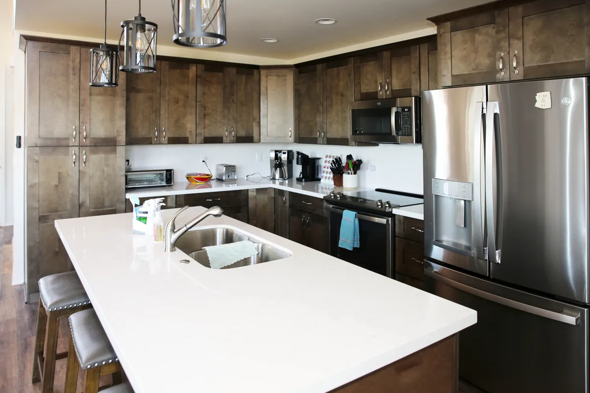 This image showcases a contemporary kitchen with a spacious island countertop, sleek stainless steel appliances, pendant lighting, and warm wooden cabinetry. The scene evokes a sense of invitation and functionality, highlighting the kitchen as a hub for meal prep and gathering.