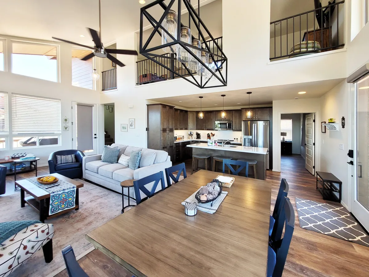 The image showcases a spacious, inviting interior featuring a grand chandelier, a large dining table ready for gatherings, a plush sofa for relaxing, and a stylish kitchen island—perfectly arranged for comfort and connection. The atmosphere is warm, cozy, and ideal for memorable family moments or festive evenings with friends.