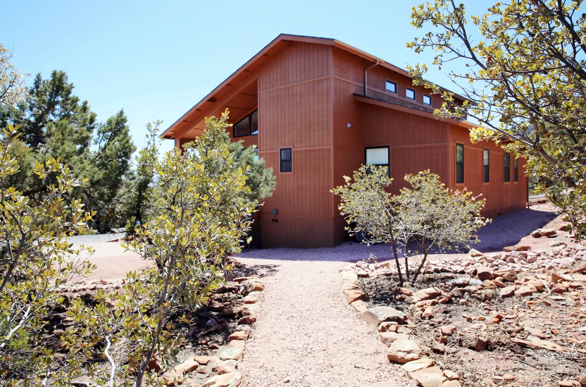 The image highlights the modern architecture of the house, with a welcoming pathway leading to the entrance, set amidst lush greenery. The tranquil outdoor scene hints at both relaxation and easy access to nature.