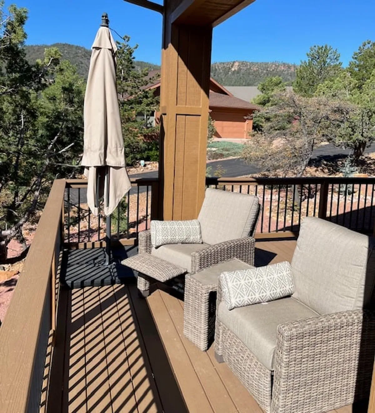 Two comfortable chairs and a parasol are arranged on a wooden deck, inviting guests to relax while overlooking the surrounding forest. The deck is elevated and bordered by nature, hinting at tranquil moments of sunrise coffees or evening stargazing in a secluded outdoor setting.