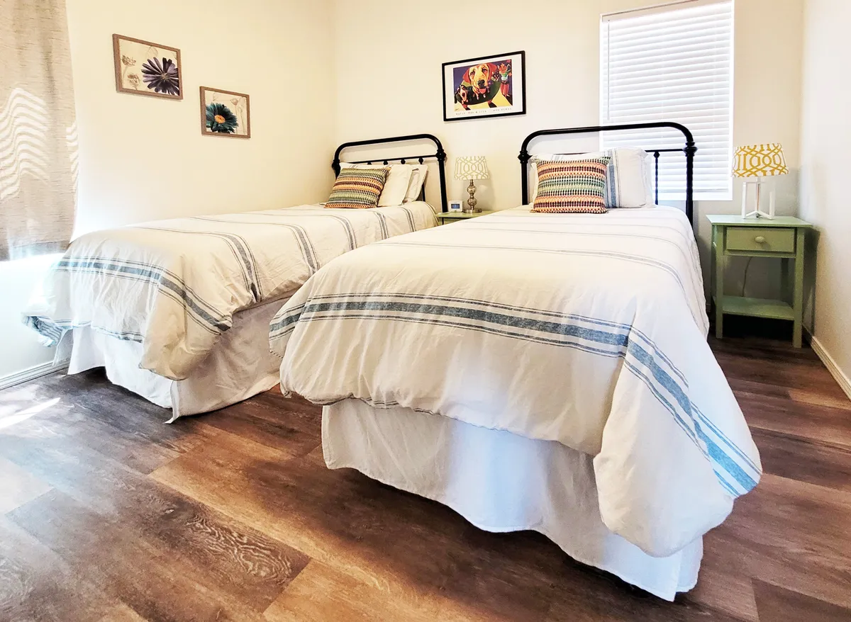 This photo presents a cheerful bedroom with two twin beds, colorful wall art, and bedside lamps. The space is airy and inviting, perfect for families or friends sharing the room.