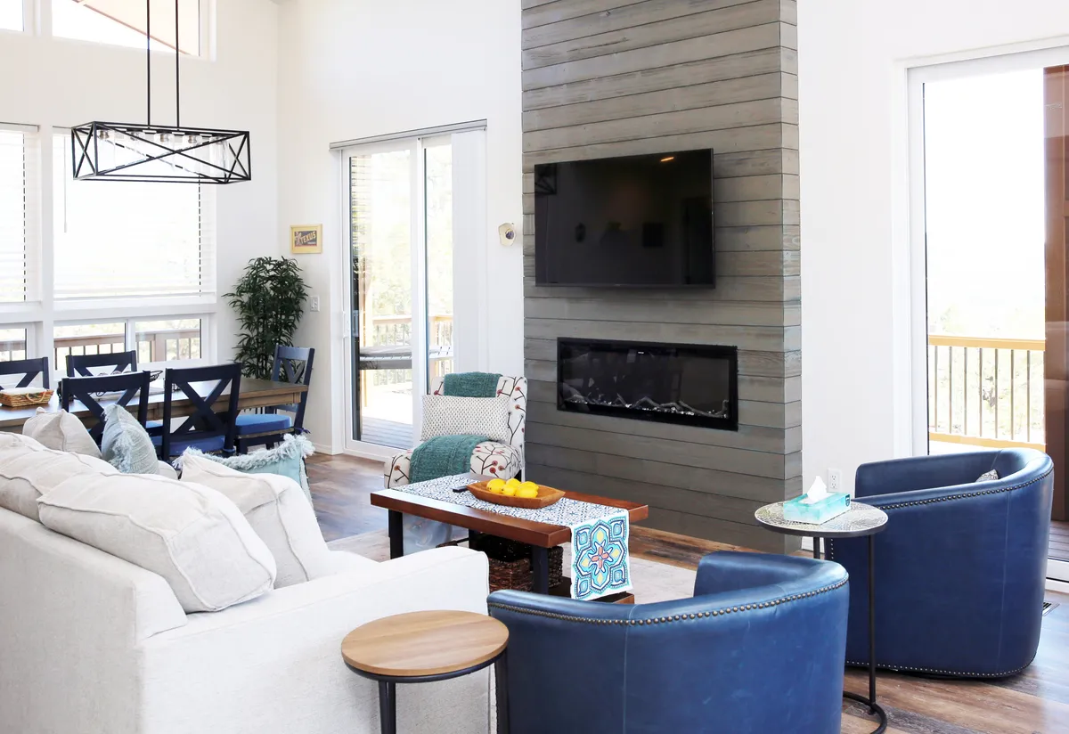 This image features a modern fireplace, a large window framing the mountainous scenery, a comfortable seating arrangement, and a dining area seamlessly connected to the living space. The décor is calming and contemporary, inviting both quiet moments and lively gatherings.