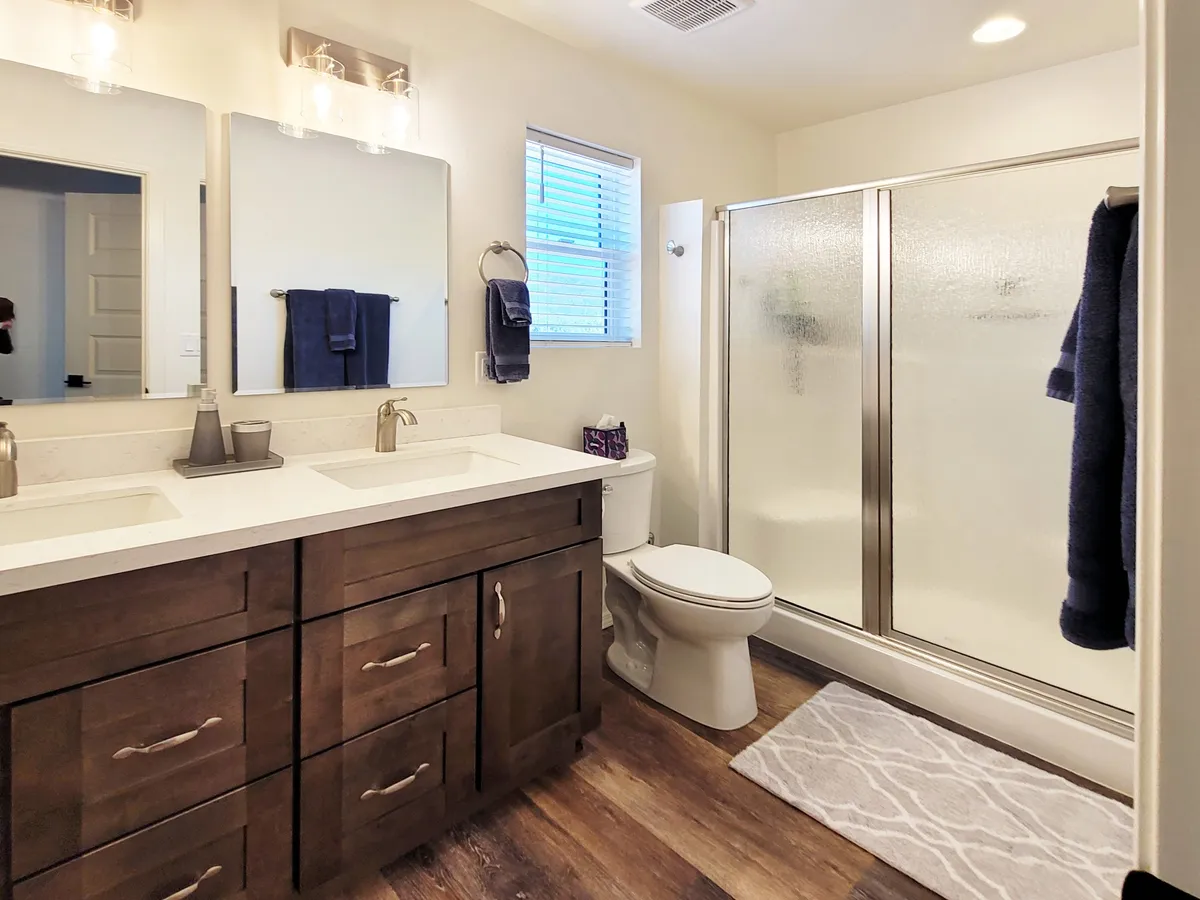The bathroom is elegantly appointed with a double sink vanity, glass shower enclosure, wooden cabinetry, mirrors, and fluffy towels. The space feels tranquil and well-organized, offering a refreshing retreat for daily routines.