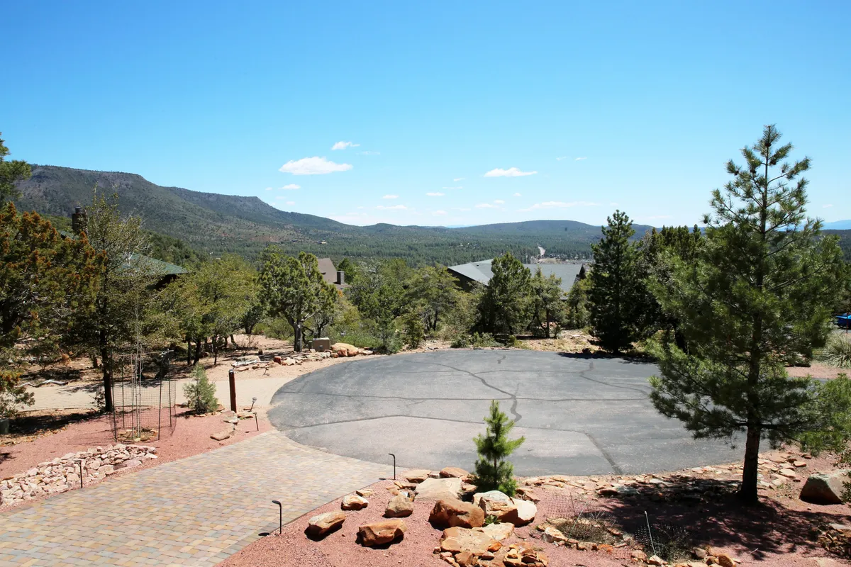 A wide circular driveway is framed by tall trees and a backdrop of mountains, offering a sense of spaciousness and connection to the outdoors. The setting is ideal for family gatherings or setting off on nearby explorations.
